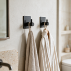 Two black adhesive robe hooks mounted on a bathroom wall holding a towel and robe