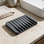 Charcoal grey self-draining silicone soap dish on a travertine bathroom vanity